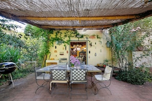 An outdoor patio with a table and chairs, surrounded by greenery and a thatched roof. - Casa Vacanze Le Camelie with Private Pool, Wi-Fi, and Air Conditioning (Vecchiano)