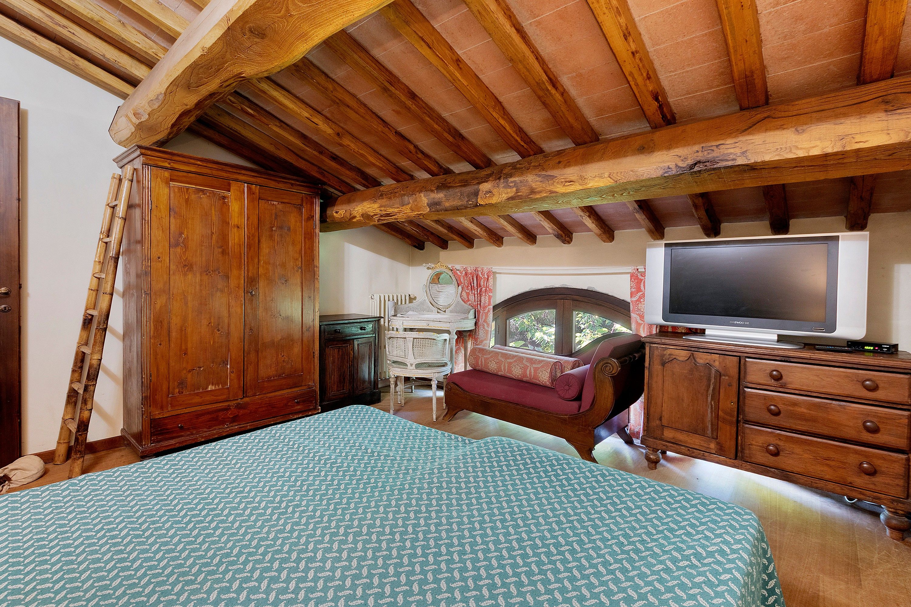 A room with a bed, wooden furniture, a television, and a window with curtains.