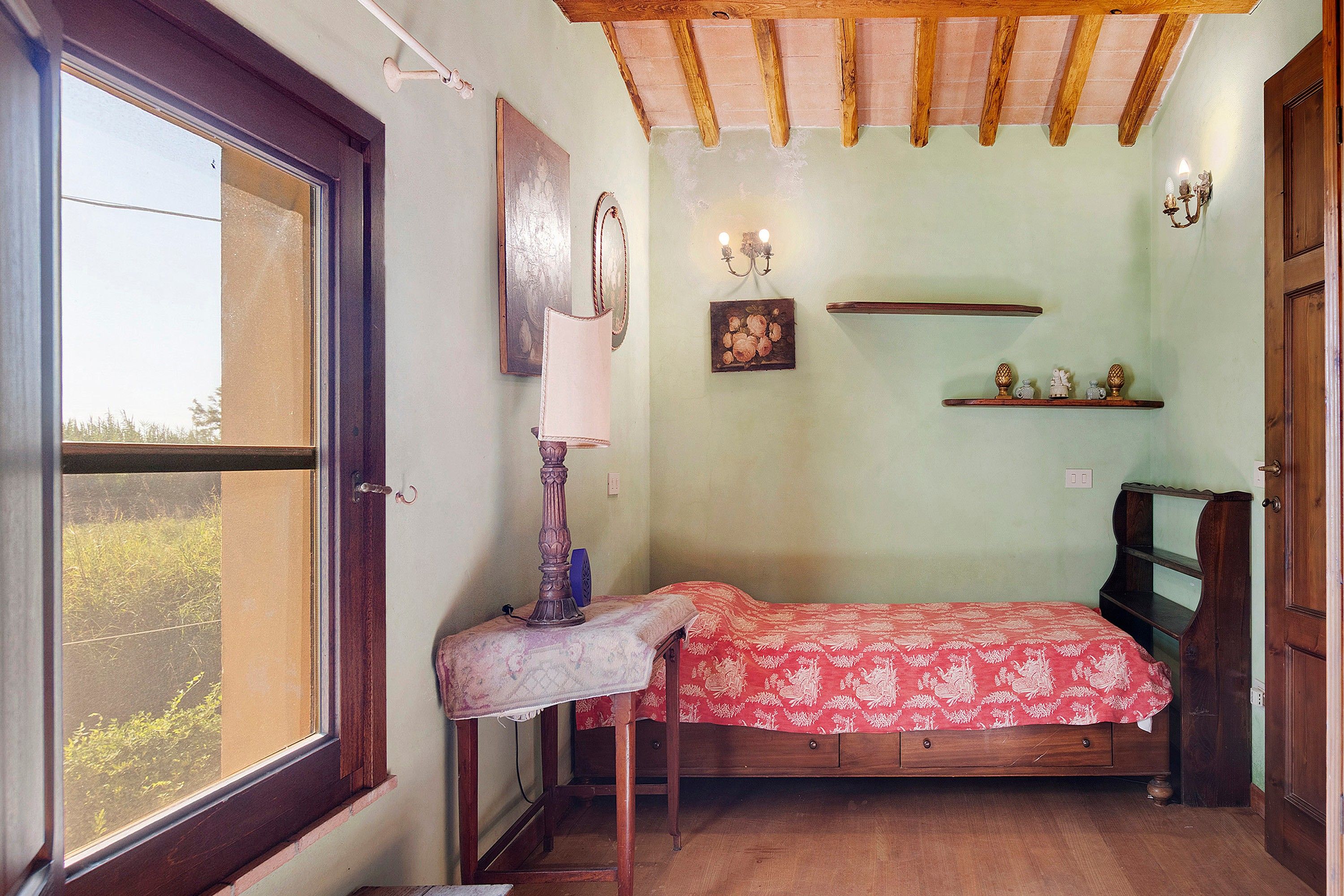 Ein kleines Schlafzimmer mit einem Einzelbett, einem Nachttisch, einem Fenster und einer Holzbalkendecke.