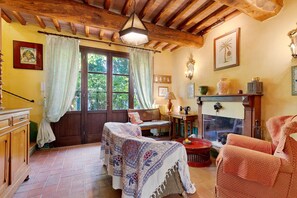 Ein gemütliches Wohnzimmer mit Kamin, Holzbalkendecke und einem großen Fenster mit Vorhängen.