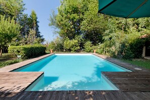 A rectangular swimming pool with a wooden deck surrounding it, set in a landscaped garden with trees and shrubs. - Casa Vacanze Le Camelie with Private Pool, Wi-Fi, and Air Conditioning (Vecchiano)