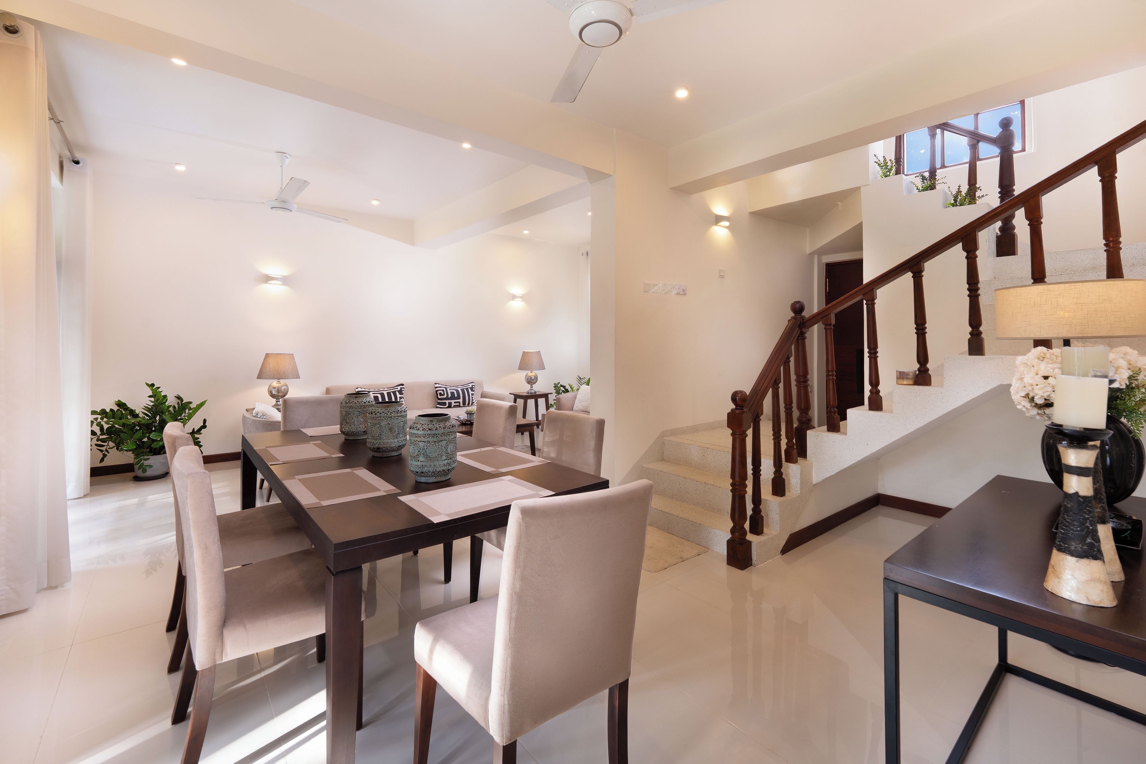 A spacious dining area with a high ceiling, a staircase with wooden railings, and a modern chandelier.