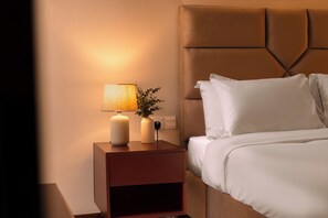 A neatly made bed with white linens, a brown headboard, and a bedside table with a lamp and a vase with green foliage. - Garden Villa for 10 people with 5 Spacious Bedrooms - Heart of Colombo (Colombo)