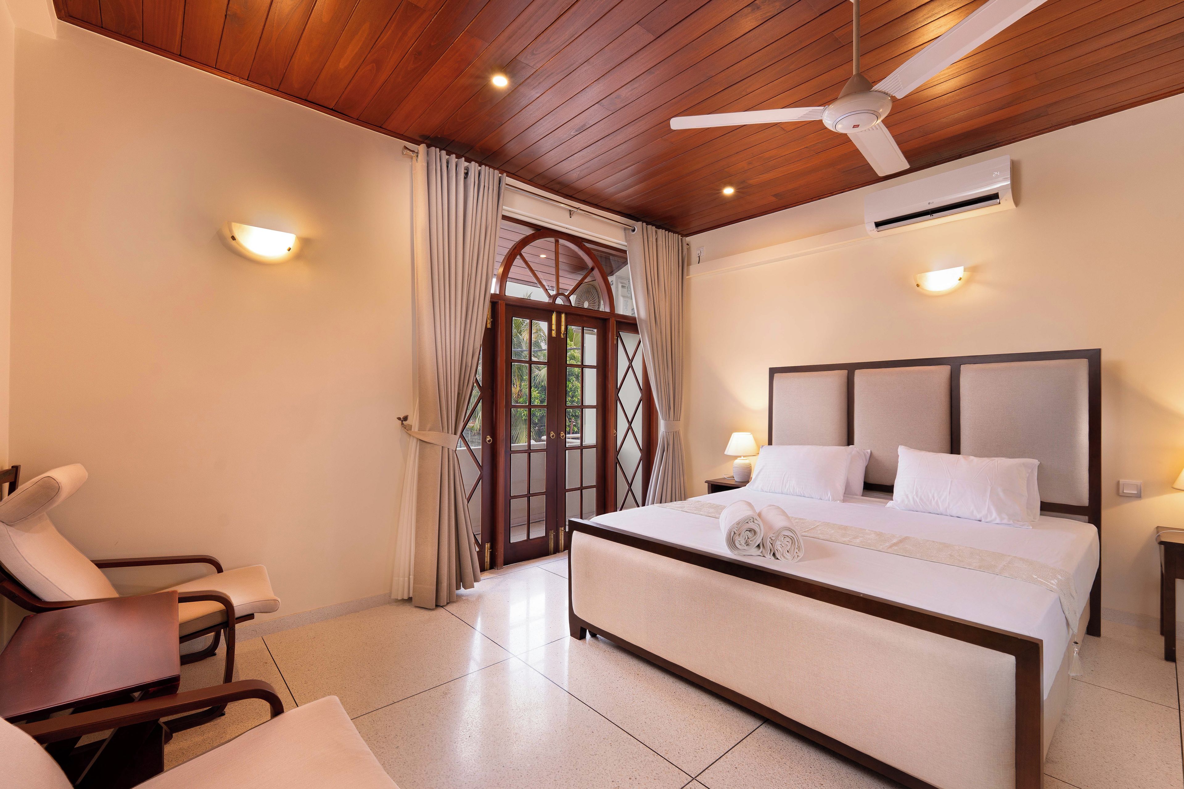 A hotel room with a bed, a chair, a ceiling fan, and a view through a door.