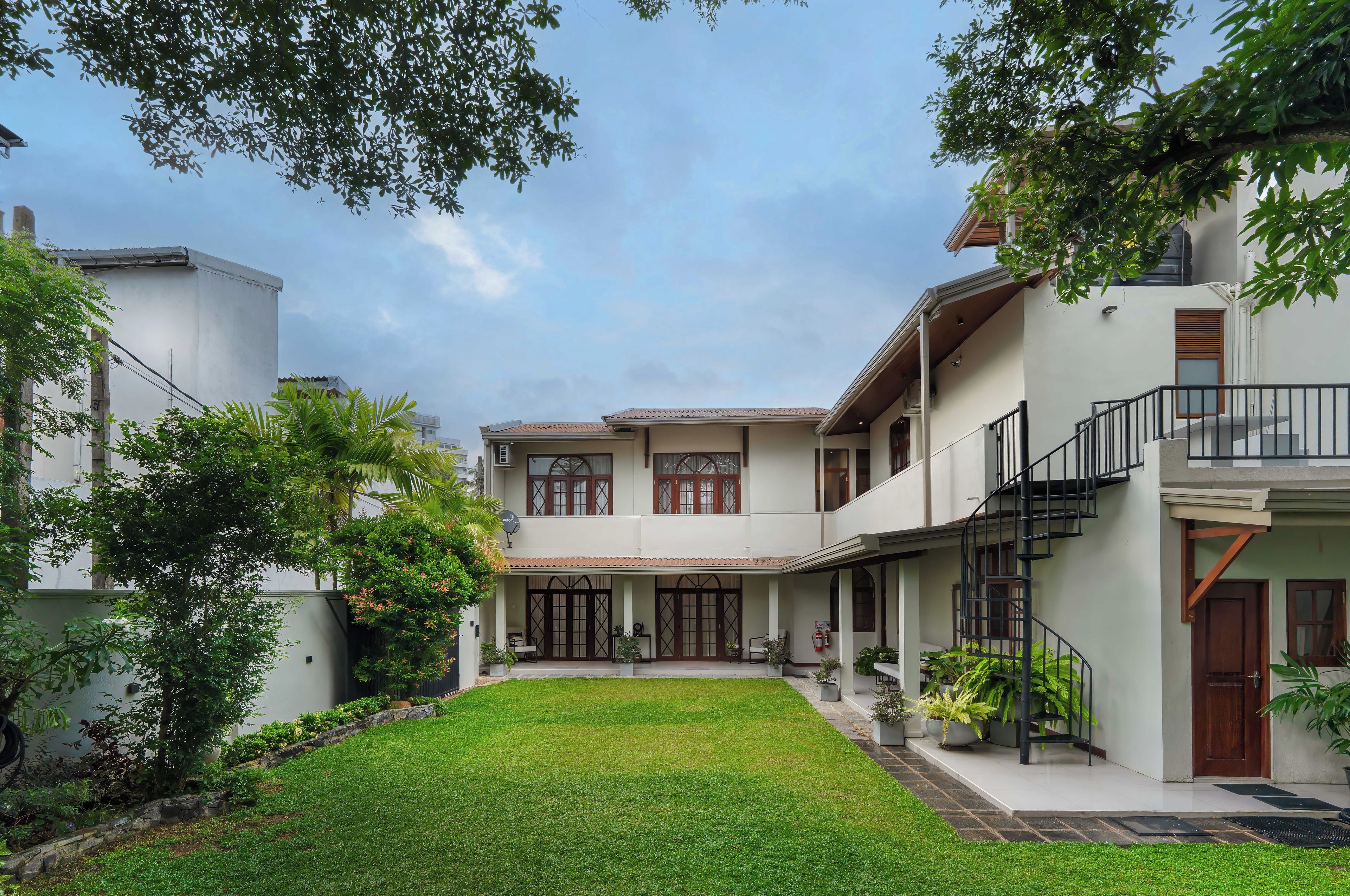 A two-story residential building with a covered patio, a small garden, and a staircase leading to an upper level.