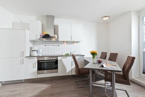 Eine moderne Küche mit weißen Schränken, einem eingebauten Backofen und einem Essbereich mit Tisch und Stühlen.