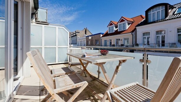 A balcony with wooden chairs and a table, overlooking a canal with buildings in the background. - Holiday apartment with 2 bedrooms (Norderney)