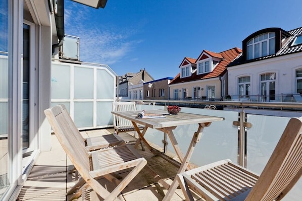 Ein Balkon mit Holzstühlen und einem Tisch, mit Blick auf einen Kanal und Gebäude im Hintergrund.