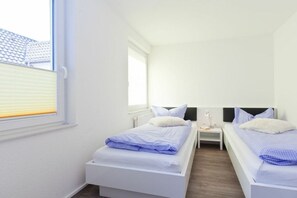 Ein Schlafzimmer mit zwei Einzelbetten, weißer Bettwäsche, einem Nachttisch mit Lampe und einem Fenster mit Jalousien.