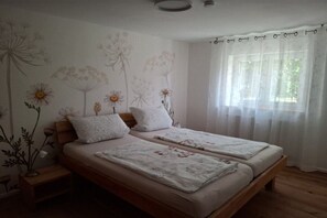 Een slaapkamer met twee bedden, een houten hoofdbord, een nachtkastje en een raam met dunne gordijnen.