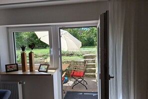 A room with a view of a garden through a glass door, a small table with a picture frame, and a chair outside. - Holiday apartment with 1 bedroom (Kemmern)