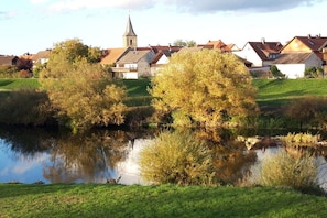 A serene lakeside setting with a church steeple, reflecting trees and buildings in the calm water. - Holiday apartment with 1 bedroom (Kemmern)