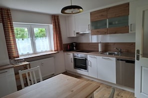 A kitchen with white cabinets, a wooden countertop, a built-in oven, a dishwasher, and a window with curtains. - Holiday apartment with 1 bedroom (Kemmern)