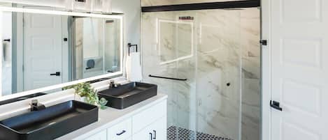 Un baño moderno con dos lavamanos, un espejo grande y una ducha con cerramiento de vidrio.
