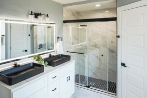Un baño moderno con dos lavamanos, un espejo grande y una ducha con cerramiento de vidrio.