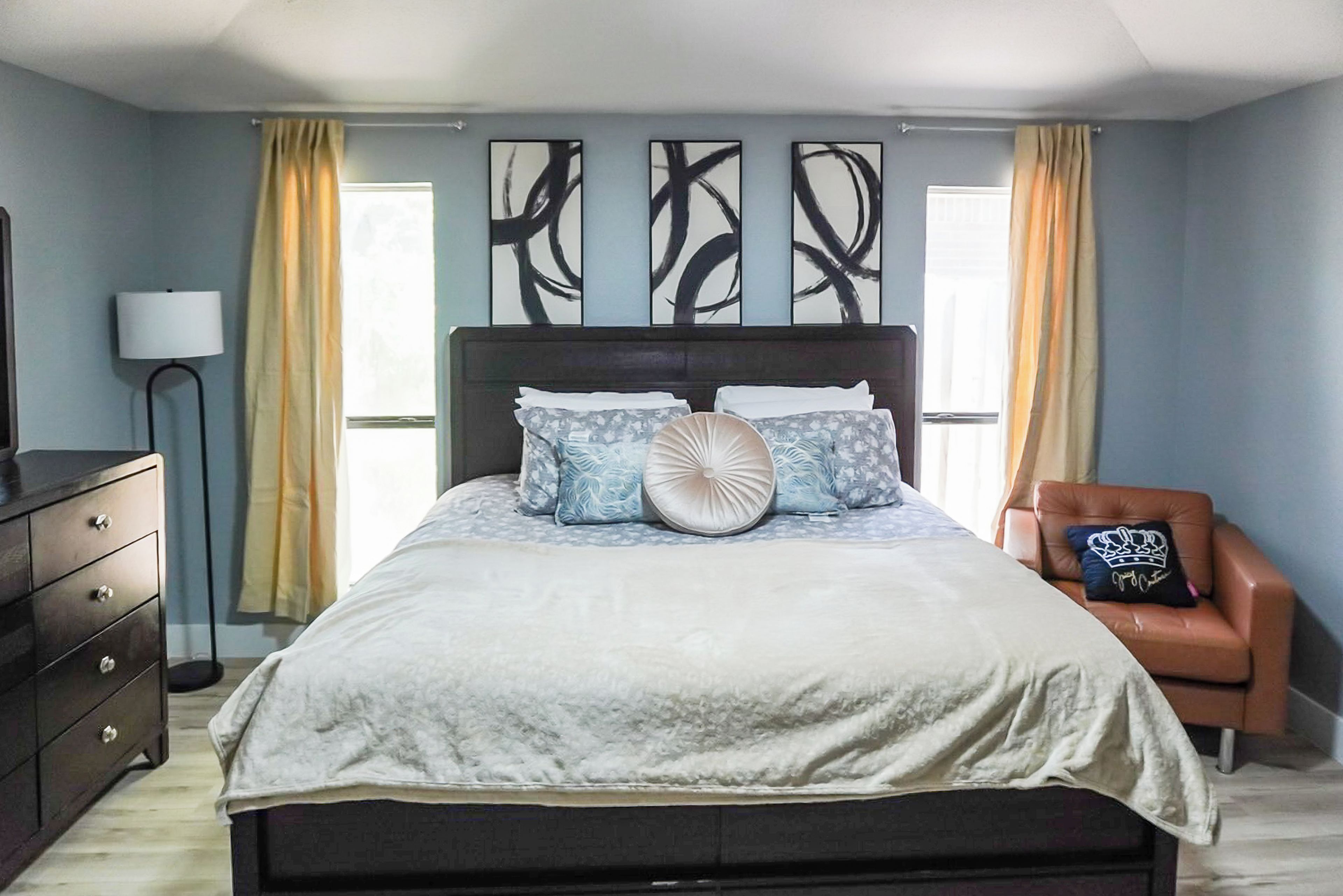 A bedroom with a bed, a dresser, a chair, and artwork on the wall.
