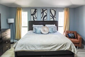 A bedroom with a bed, a dresser, a chair, and artwork on the wall.
