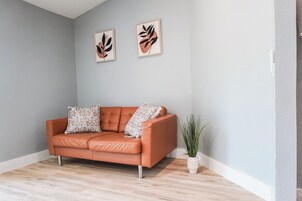 Una habitación con pared gris claro, un sofá de cuero marrón con cojines estampados y dos cuadros abstractos enmarcados.