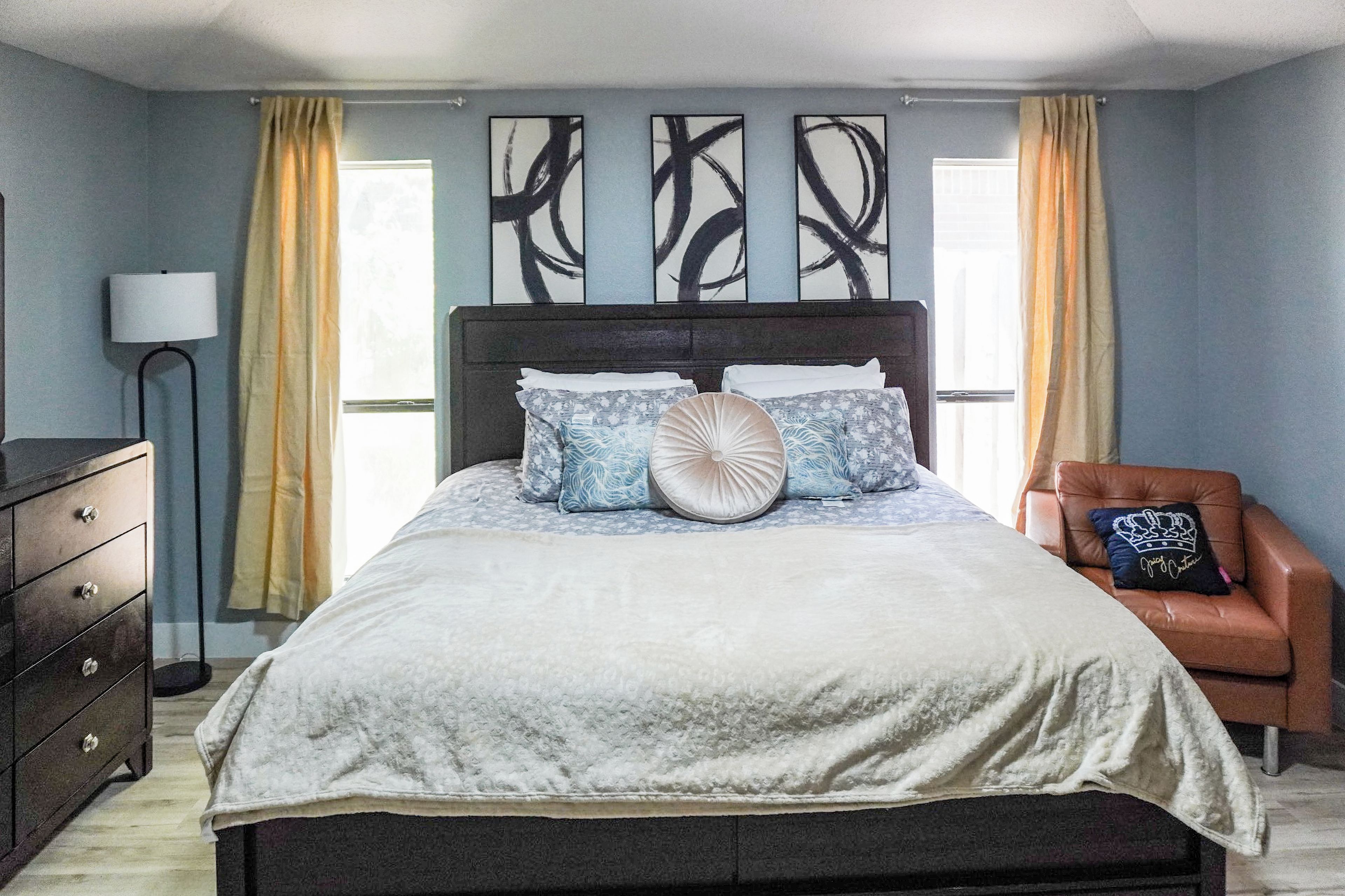 A bedroom with a bed, a dresser, a chair, and artwork on the wall.