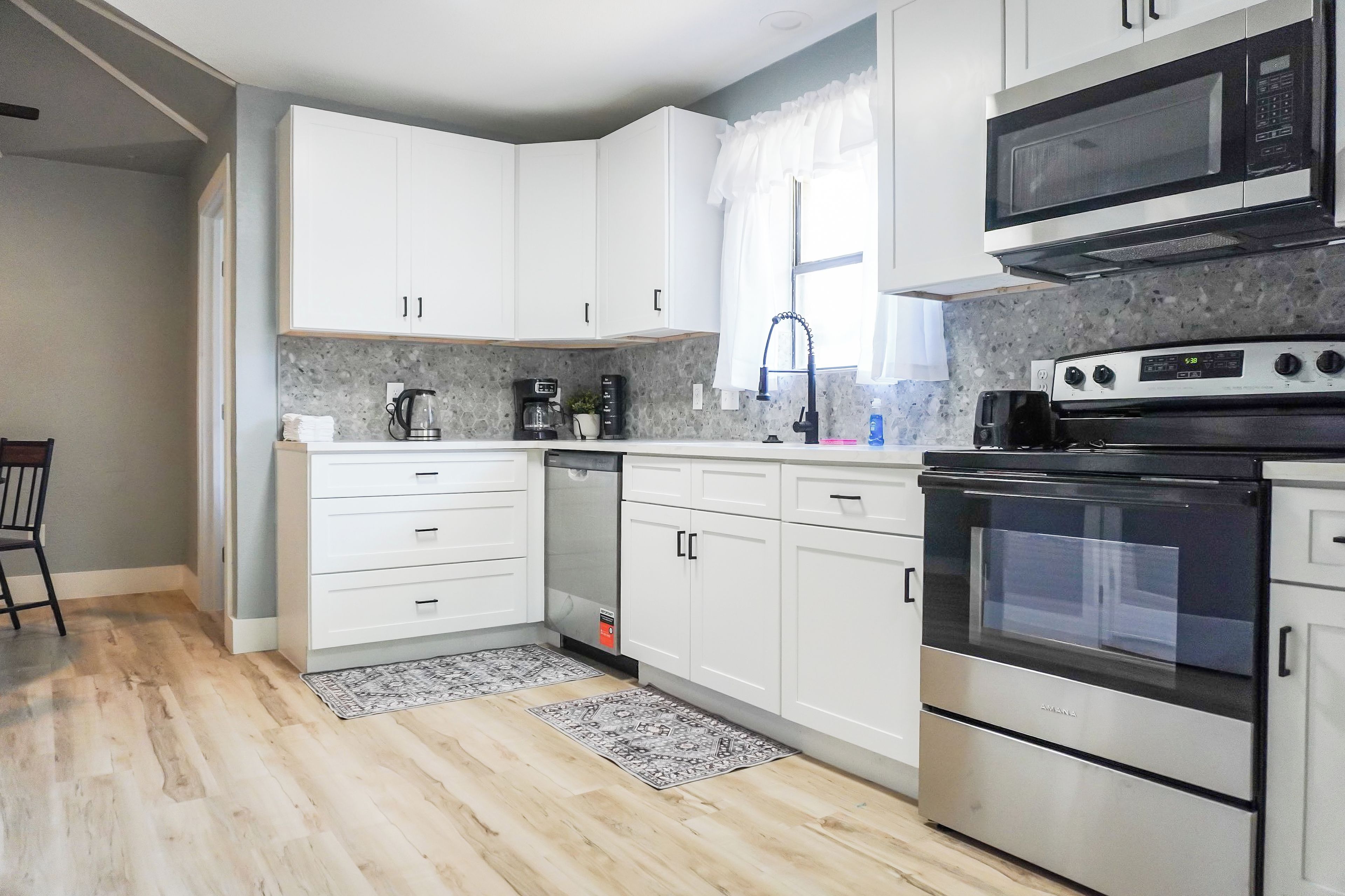 A modern kitchen with white cabinets, a built-in microwave, a stove, and a coffee maker.