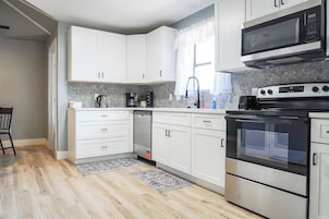 Una cocina moderna con armarios blancos, microondas integrado, estufa y cafetera.