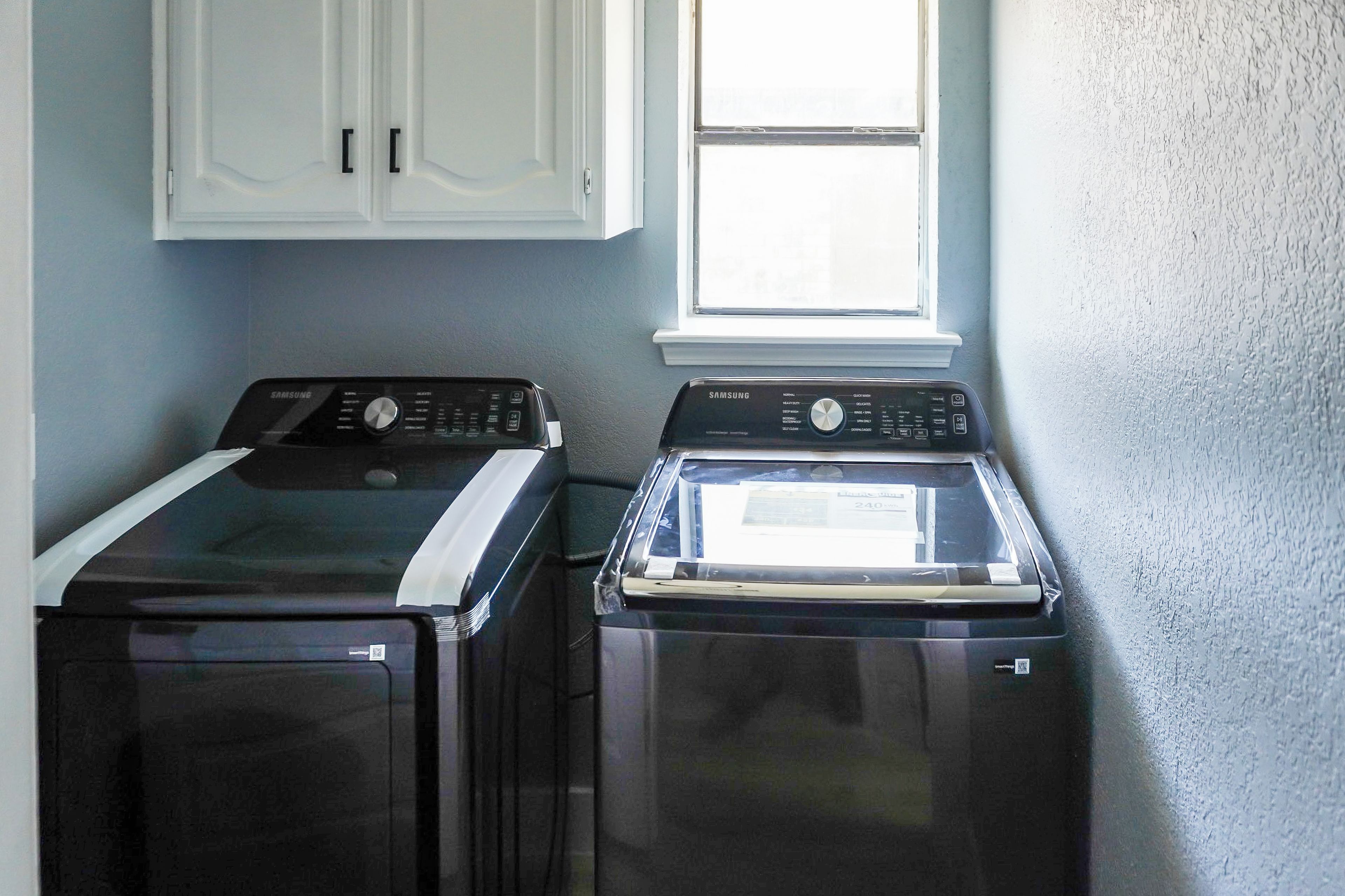 A laundry room with two front-loading washers and a window above.
