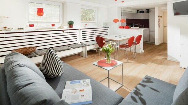 En moderne stue med sofa, sofabord og spiseplads med røde stole.