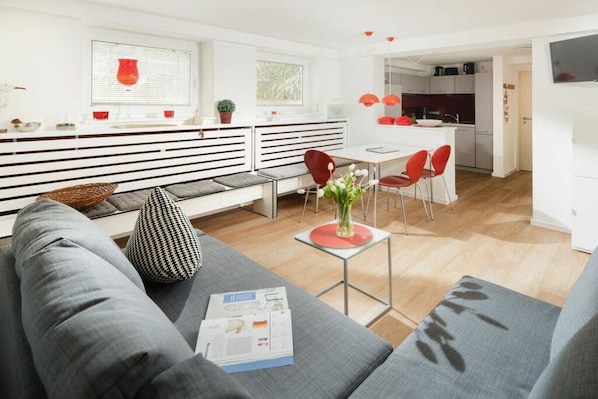 Ein modernes Wohnzimmer mit einer Couch, einem Couchtisch und einem Essbereich mit roten Stühlen.