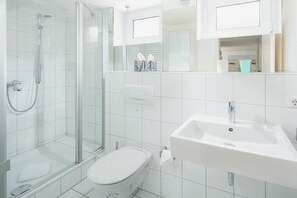 Ein modernes Badezimmer mit einer gläsernen Duschkabine, einer weißen Toilette und einem Waschbecken mit Spiegel darüber.