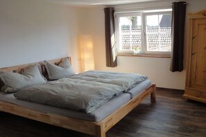 A bedroom with a wooden bed, a window with curtains, and a wooden wardrobe. - Black Forest Lounge Holiday Home Lindenbuch (Loßburg)