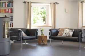 A modern living room with two leather sofas, a coffee table, a bookshelf, and a window with curtains. - Black Forest Lounge Holiday Home Lindenbuch (Loßburg)