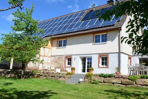 A house with a solar panel roof, a stone wall, and a well-maintained lawn. - Black Forest Lounge Holiday Home Lindenbuch (Loßburg)