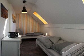 A room with a sloped ceiling, a bed, a bedside table, a lamp, and a window. - Holiday apartment with 1 bedroom (Heiligenhafen)