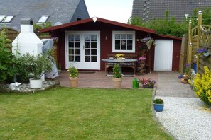 A house with a red roof, white doors, and a garden with potted plants and a table. - Holiday apartment with 1 bedroom (Heiligenhafen)