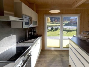 A kitchen with a stove, microwave, and cabinets, and a sliding glass door leading to a view of a green landscape. - One-bedroom Cabin (Sankt Georgen am Kreischberg)