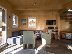Ein Holzinterieur mit einer Couch, zwei Sesseln, einem Fernseher und einer verzierten Kommode.