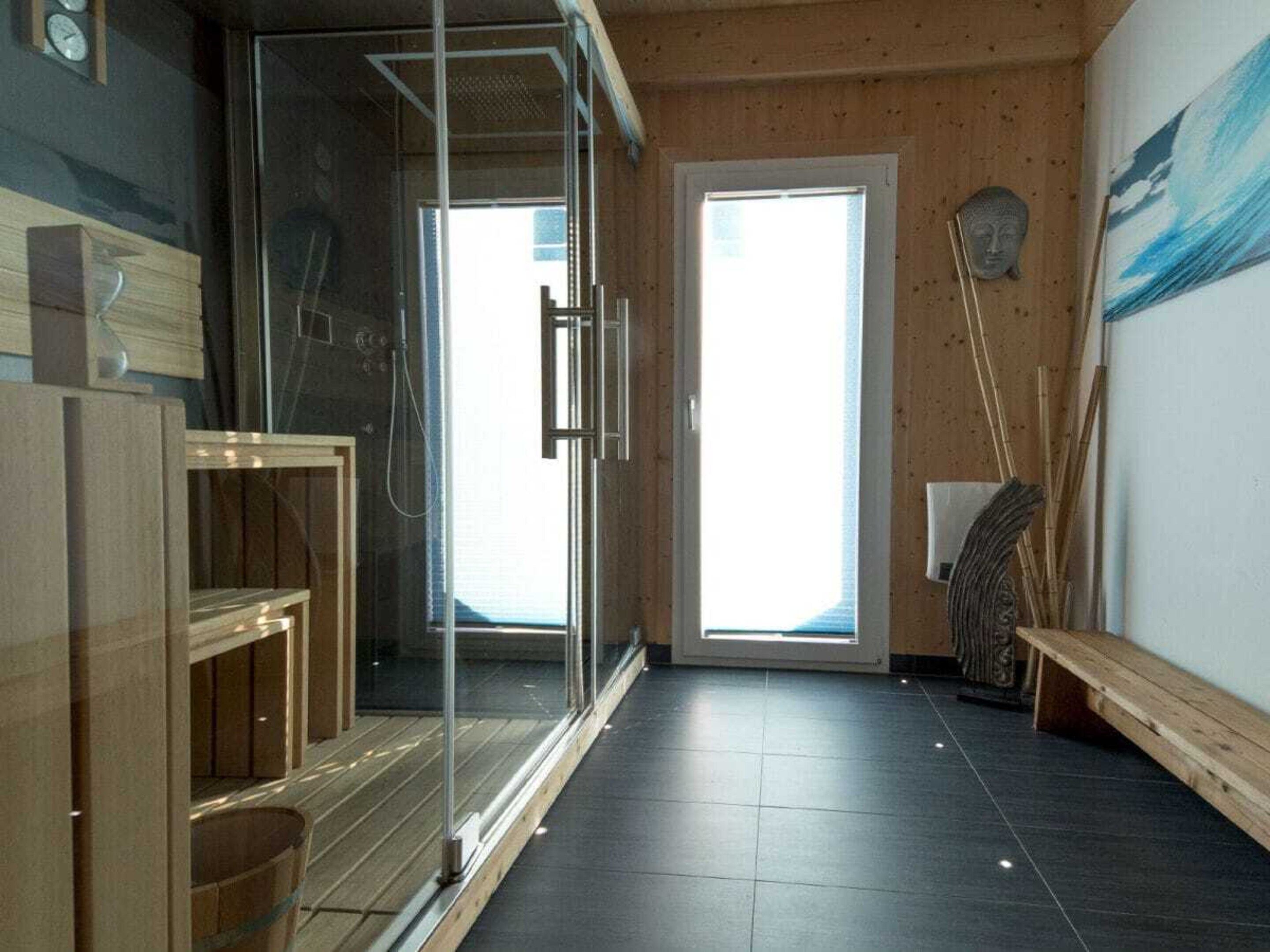 A modern bathroom with a glass shower enclosure, wooden flooring, and a large window providing natural light.