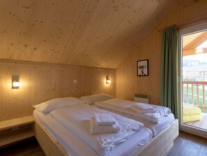 A wooden room with a bed, two wall-mounted lights, a framed picture, and a window with curtains. - One-bedroom Cabin (Sankt Georgen am Kreischberg)