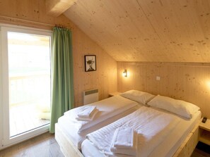 Ein Zimmer mit einem Bett, einem Vorhangfenster, einer Wandleuchte und einem gerahmten Bild.