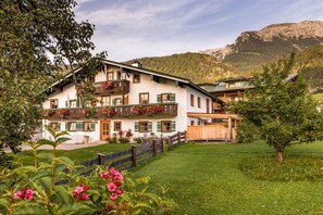 A traditional chalet with a balcony, surrounded by lush greenery and mountains in the background. - Unterbrandnerlehen FeWo Königssee (Königssee)