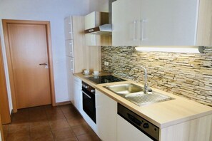 A compact kitchen with a built-in dishwasher, a double sink, and a stone backsplash.
