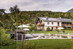A house with a solar panel roof, a swimming pool, and a garden with lounge chairs.