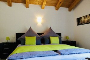 A bedroom with a bed, two nightstands, a wall-mounted light, and a painting.