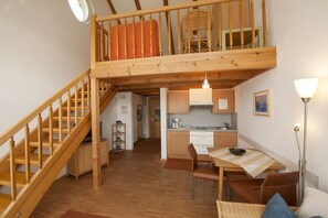 A loft-style room with a wooden staircase, a kitchen area, and a dining space. - Holiday apartment with 1 bedroom (Lindau(B))