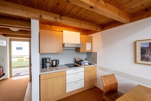 A compact kitchen with wooden cabinets, a countertop, and a single chair. - Holiday apartment with 1 bedroom (Lindau(B))