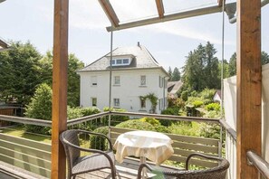 A balcony with wicker furniture and a table, overlooking a house and greenery. - Holiday apartment with 1 bedroom (Lindau(B))