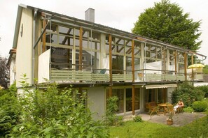 Ein zweistöckiges Haus mit Balkon, großen Fenstern und einem Garten.