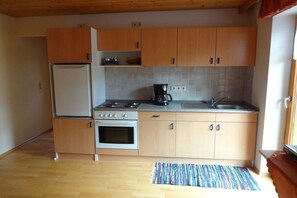 A compact kitchen with wooden cabinets, a refrigerator, a stove, and a coffee maker. - Holiday apartment in Böbrach with Wi-Fi (Böbrach)
