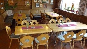 Interior de restaurante com mesas e cadeiras de madeira, área de banco e quadros nas paredes.