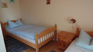 Uma cama de solteiro com estrutura de madeira e mesa de cabeceira combinando, uma pequena mesinha de apoio e uma luminária fixada na parede.